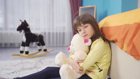 Unhappy-and-thoughtful-little-girl-hugging-her-teddy-bear-in-her-room.